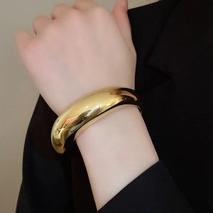 Gros plan d'un bracelet ovale doré poli porté sur une manchette de blazer noir pour femme
