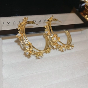 Macro shot of gold-plated triple hoop earrings with floral accents and white pearls
