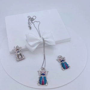 Detail of silver insect jewelry set featuring zircon inlay on white display stand