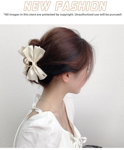 Close-up of a cream-colored satin bow hair claw clip with golden metal accents on a model