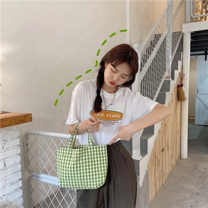 Detail shot of a green checkered linen lunch bag held by a model in a cafe setting