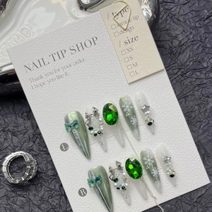 Macro shot of green cat-eye press-on nails with emerald gems and white snowflakes