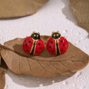 Boucles d'oreilles coccinelle rouges en acier inoxydable sur fond de feuille rustique