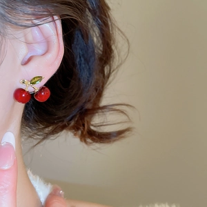 Close-up of red cherry earring with gold stem and green zircon leaf on model's ear