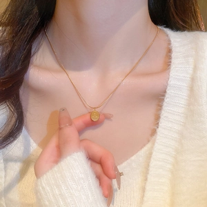 Détail d'un collier chaîne serpent dorée avec un pendentif ovale gravé sur un mannequin