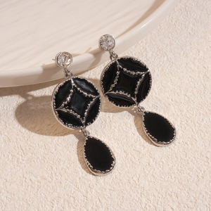 Macro shot of black enamel star earrings with drop pendants on a white ceramic plate