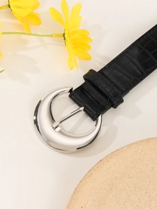Close-up of black crocodile pattern belt with a silver circular metal buckle for jeans