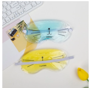 Blue and yellow cat gel eye masks with elastic straps on a minimalist workspace background