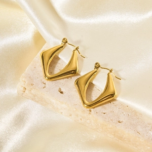 Dettaglio orecchini geometrici in acciaio inossidabile oro 18K su pietra beige e seta