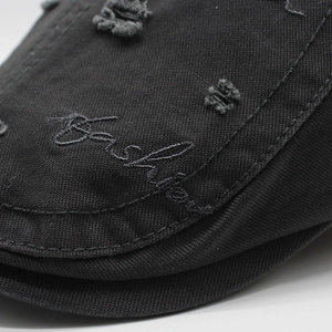 Close-up of black cotton beret featuring distressed fabric and Fashion embroidery