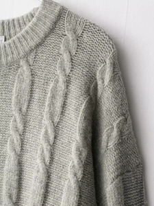 Detailed close-up of grey cable knit sweater neckline showing thick textured braided wool