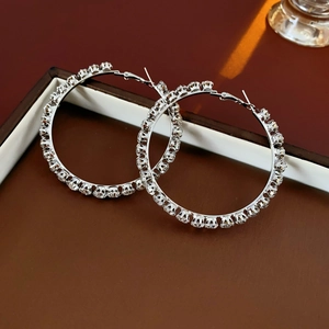 Detailed close-up of large silver hoop earrings with clear rhinestones on a brown tray