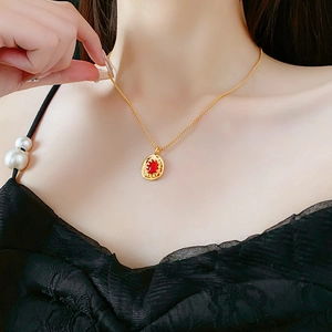Close-up of vintage oval necklace with red gemstone and gold beaded detail