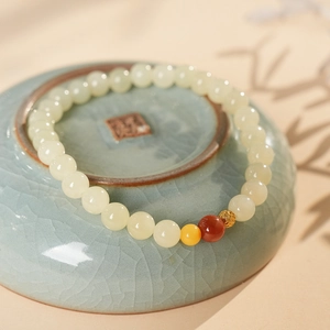 Macro shot of faux Hetian jade beaded bracelet with hollow gold bead on celadon plate