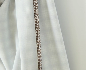 Detalle de tela texturizada clara con costuras overlock marrones en el dobladillo de la falda