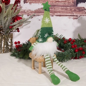 Close-up of green knitted Christmas gnome sitting on a mini wooden chair with festive decor