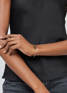 Detail of an open gold bangle with two green square gemstones worn on a model wrist