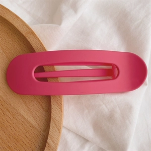 Close-up of a rose red matte hair clip with a smooth oval design on a wooden tray