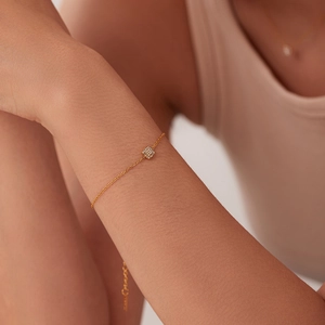 Detail eines filigranen 18K vergoldeten Armbands mit quadratischem Zirkonia-Anhänger am Handgelenk