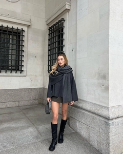 Full view of asymmetric charcoal knit shawl with black boots in a classic street setting
