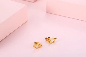 Macro shot of stylish golden eye-shaped stud earrings on a pink background