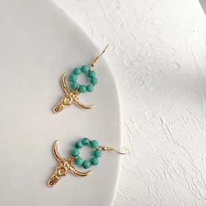 Detail of bohemian gold earrings with turquoise beads and bull skull charms on stone