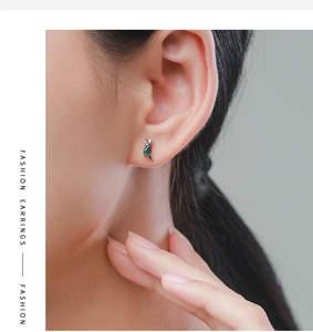 Close-up of small S925 silver dinosaur stud earring with a green gemstone on ear