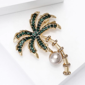 Detail of golden coconut tree brooch with green crystals and a white pearl on white base