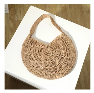 Top view of a beige handcrafted round woven straw bag on a white platform and wooden floor