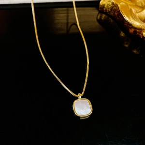 Gros plan d'un collier doré avec pendentif carré en nacre aux reflets irisés élégants