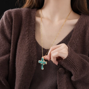 Detail of cross pendant necklace with teal gemstone on model wearing brown sweater