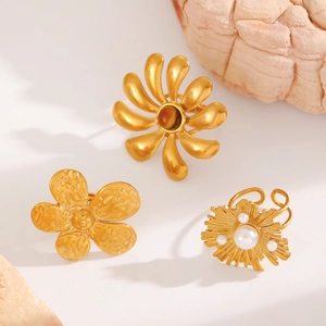 Close-up of gold flower rings with pearl detail and hammered texture on stone base