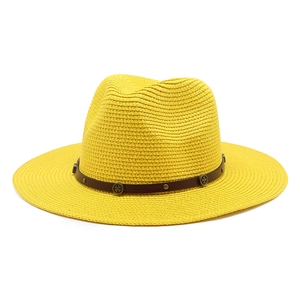 Close-up of yellow woven straw fedora hat featuring brown leather band with metal studs