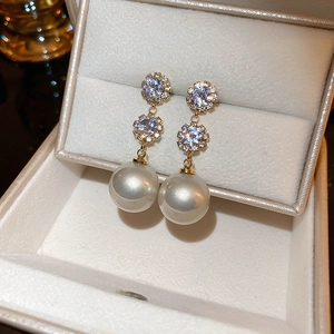 Détail de boucles d'oreilles fleur dorées avec diamants et perles dans un écrin à bijoux