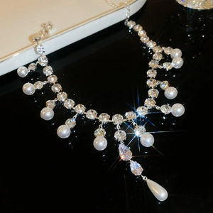 Macro detail of silver necklace with shiny rhinestones and round white pearls on black background