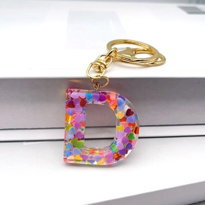 Detail of a transparent resin D-letter keychain with colorful heart-shaped sequins and gold hardware