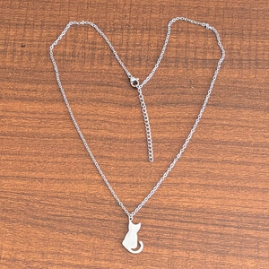 Pendentif silhouette de chat en acier poli sur chaîne sur fond de bois marron