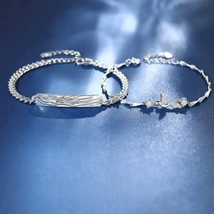 Detail of silver couple bracelets with bird and mountain charms on a dark blue background