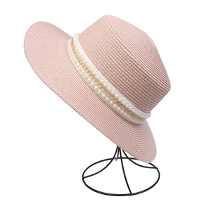 Detail of pink straw hat featuring delicate pearl and gold chain decorative band