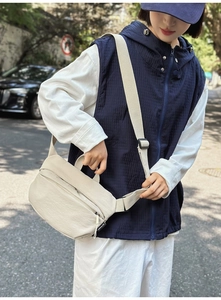 Outdoor street style shot of a beige nylon crossbody bag with adjustable strap and front pocket