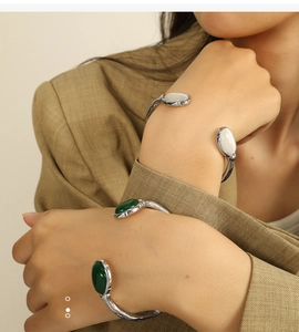Detail view of silver open cuff bracelets with white and green oval gemstones on a wrist