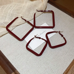 Macro detail of glossy burgundy geometric square hoop earrings in two sizes on linen