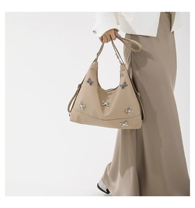 Detail of khaki shoulder bag with silver butterfly metal charms held by a model