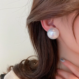 Close-up of elegant oversized round pearl stud earring with iridescent sheen on model