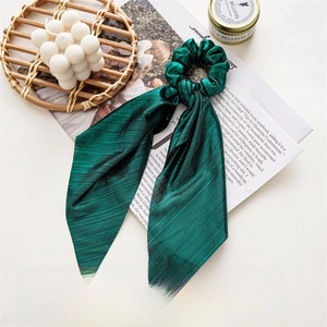 Detail of dark green fabric scrunchie with long ribbons and elegant metal sheen texture