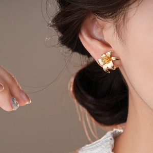 Close-up of elegant gold flower stud earring with textured petals on female model's ear