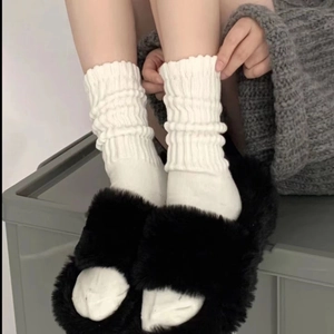 Detail of white slouch socks with knitted texture paired with black slippers