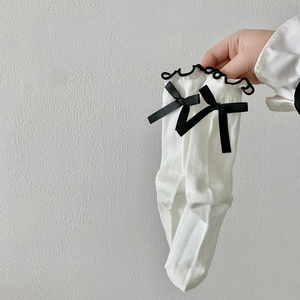 Close-up of white ribbed socks with black wavy lace trim and elegant black bows