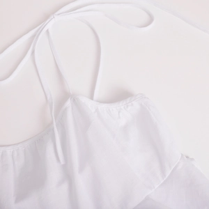 Detailed macro view of white tiered dress featuring a drawstring neckline and woven fabric texture
