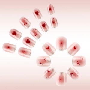 Close-up of pink press-on nails featuring red hearts, silver glitter, and star patterns